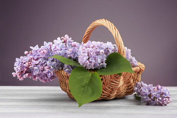 Fototapeta na wymiar Wicker basket with beautiful lilac flowers on wooden table