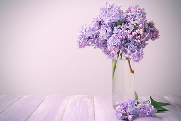 Vase with beautiful bouquet of lilac flowers on light background