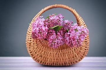 Fototapeta na wymiar Wicker basket with beautiful lilac flowers on wooden table