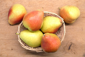 Red and yellow pears lays in small wicker straw basket on brown wooden table top view closeup