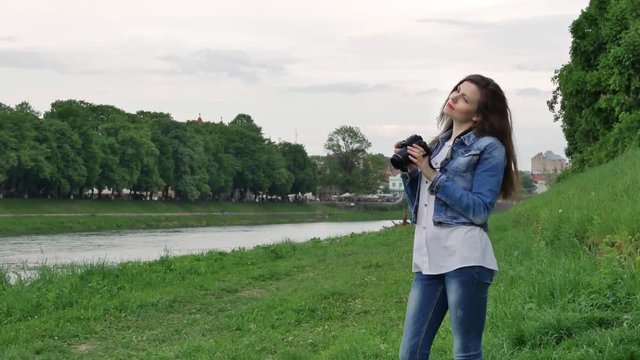 Beautiful girl tourist taking photos with a professional camera on the banks of the river in windy weather