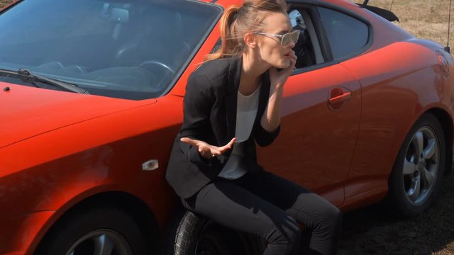 girl sits on the spare wheel of the car and talking on the phone
