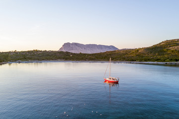 Aerial view of a sailboat in a bay of the Emerald coast at sunset in Sardinia, Italy.