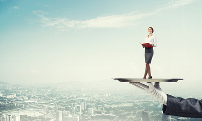 Attractive businesswoman on metal tray with red book in hands against cityscape background