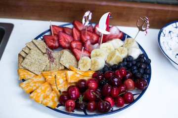 Plate with fruit and snack. Cheese, cracers, cherry, strawberry, blueberry, banana, snakcs. Nautical toothpicks