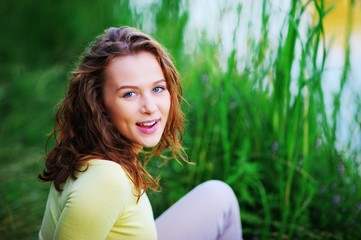 Portrait of a beautiful happy woman sitting on a green lawn in summer, on blurred grass background, closeup.