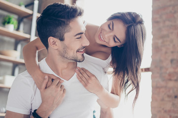 Beautiful couple of young lovers are hugging indoors at home, looking at each other with love and...