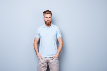 Fototapeta premium Confident serious handsome red bearded young man in casual stylish outfit, standing on the pure background, hands are in pockets
