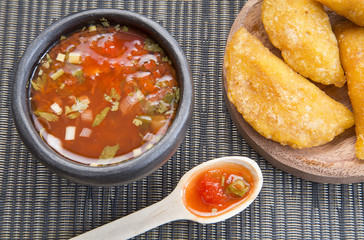 Colombian empanada with spicy sauce on wooden background