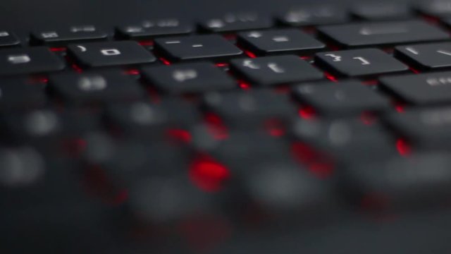 Angled Close up move right to left over back lit laptop keyboard with red nahimic RGB keys shining from below 