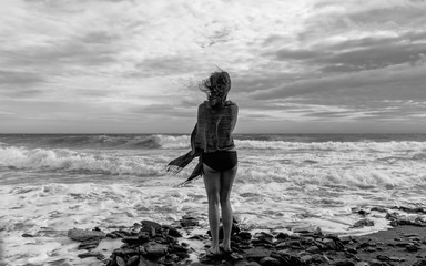 Young woman on the beach looking at waves black and white