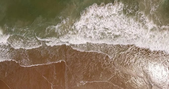 A unique aerial top-down view of the daytime ocean surf hitting against a sandy beach.	 	