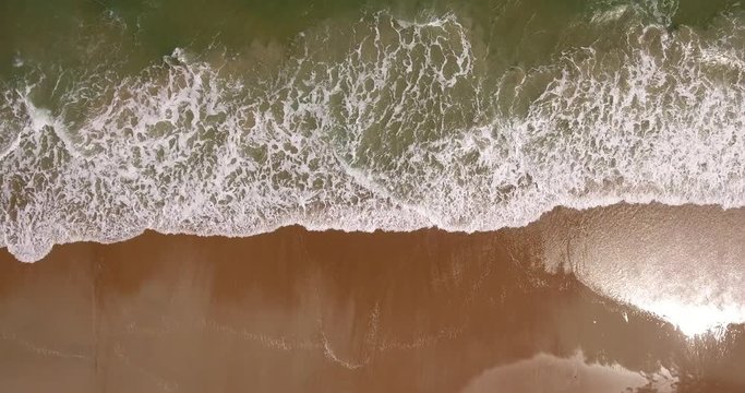 A unique aerial top-down view of the daytime ocean surf hitting against a sandy beach.	 	