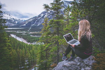Girl with a laptop working on the top of the mountain