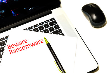 Close-up handwriting word beware ransomware on white paper over laptop with map of global ransomware cyber attack background. Cyber security concept.