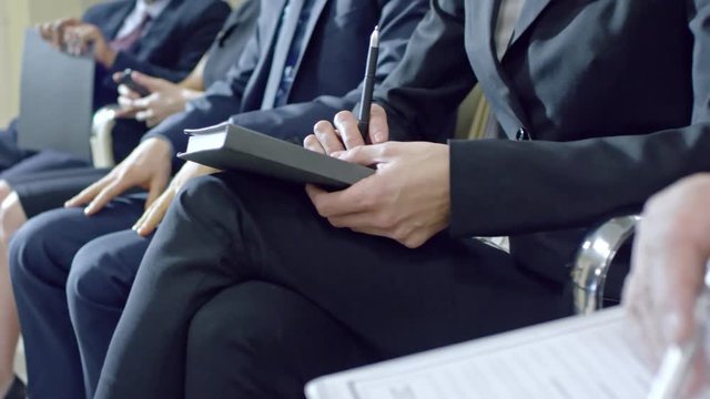 Tracking slow motion shot of businessmen and woman sitting in queue while waiting for job interview. Man filling application form and woman using smart phone