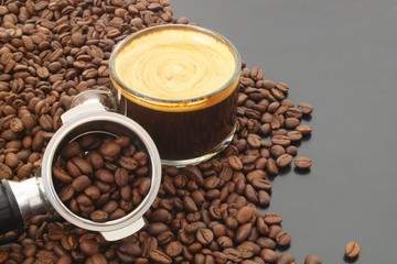 Cup of espresso coffee, coffee machine portafilter and roasted coffee beans on table