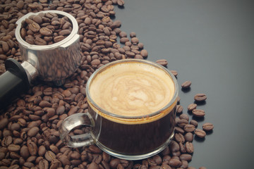 Cup of espresso coffee, coffee machine portafilter and roasted coffee beans on table