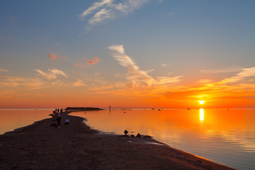 Colorful sunset over sand coast of the sea. People enjoying dawn