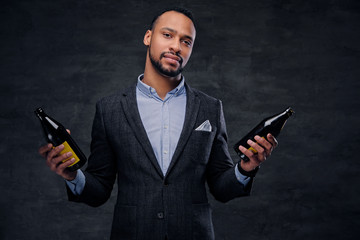 Studio portrait of elegant black male in a suit holds beer bottles.