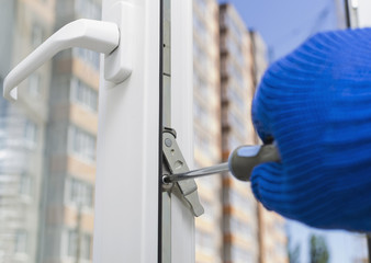 Construction worker installing new plastic window in house. Adjusting the lock with a screwdriver.