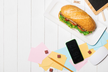Snack at break time. Healthy business lunch in office, top view of Vietnamese sandwich, or Ban Mi on white wooden desk with coffee, mobile phone and notepad with pen flat lay.