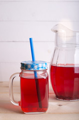 Fresh and healthy red Fruit juice drink  in a glass and jug on the wooden white table background. Side view.