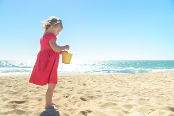 Little blond girl in red dress on the beach