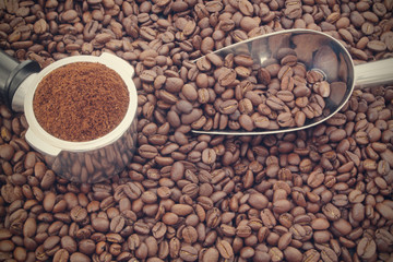 Ground coffee in portafilter and metallic shovel on roasted arabica coffee beans, espresso coffee concept