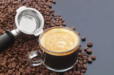 Cup of espresso coffee, coffee machine portafilter and roasted arabica beans on table