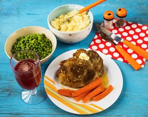 Baked pork meat, peas, couscous, vegetable, cutlery, drink. On wooden blue background.