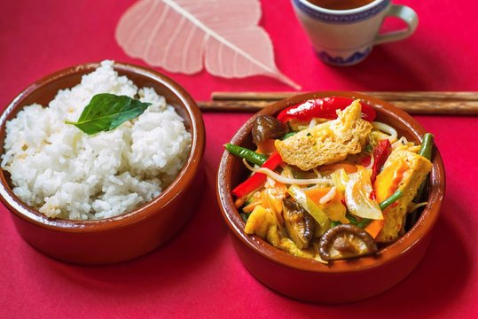 Fried tofu, vegetable and mushroom, rice, tea, chopstick. On red background.