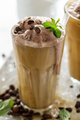 Tasty cold refreshing drink with coffee, milk, chocolate ice cream and ice in glass on ice background. Closeup.