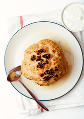 Whole roasted cauliflower with goat cheese sauce on ceramic plate on white background