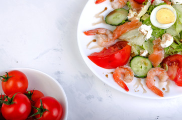 Salad with vegetables and shrimps in a white dish. On a light background.