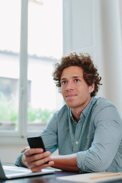 Young free lancer holding mobile phone sitting at desk