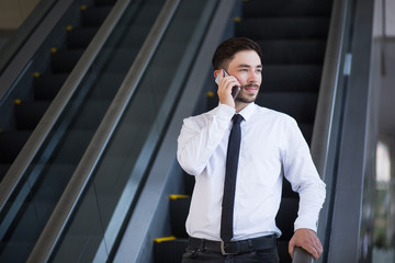 Pensive man with phone moving down on escalator
