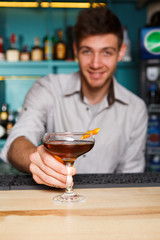 Young Barman offers alcohol cocktail in night club bar