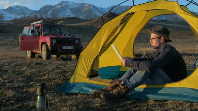 Handsome young man tourist using cell phone and portable mini speaker in touristic tent 20s 4k