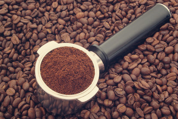 Ground coffee in coffee maker portafilter on coffee beans background, espresso symbol
