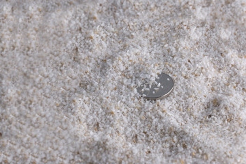 Silver coin on sand from seashells, sandy background