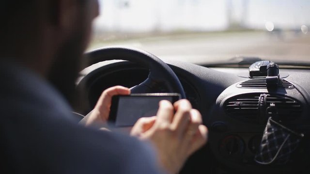 A man with a beard paves the route on a smartphone while sitting in the car