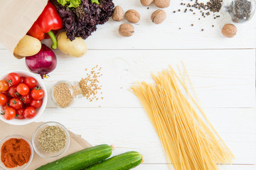 Top view of uncooked spaghetti and fresh raw vegetables and spices on wooden table