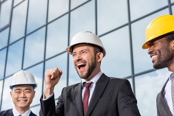 multiethnic group of excited professional architects in helmets outside office building, architects meeting concept