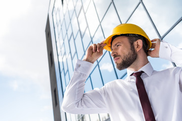 side view of confident professional architect in hard hat against building