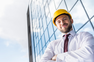 portrait of smiling professional architect in hard hat against building