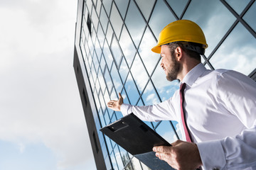 side view of professional architect in hard hat holding folder and gesturing