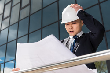portrait of confused professional architect in hard hat looking at blueprint