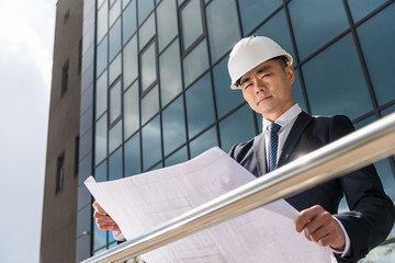 portrait of serious professional architect in hard hat looking at blueprint