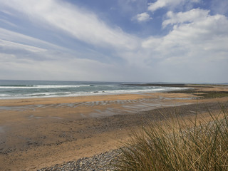 Beach landscape scene with ocean, blue cloudy sky and yellow sand.